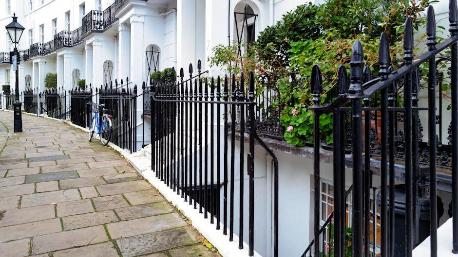 A residential street in South Kensington lined with parked cars on both sides. The street features elegant Victorian-style townhouses with white facades and decorative architectural details. Pink cher