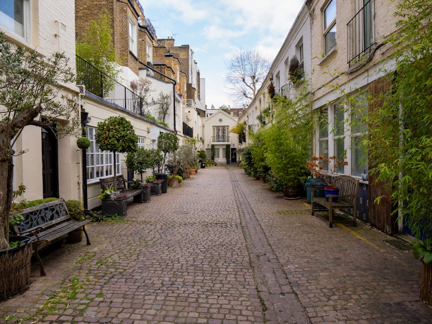 A blue bicycle with a black front basket is parked and locked to a black wrought iron fence along a stone-paved sidewalk outside white terraced residential buildings. The surfaces, including the fence, pavement, and building steps, appear clean and well-maintained, with no visible dirt or debris. The image showcases an orderly street scene in South Kensington, with natural lighting highlighting the shine of the bicycle and the neat appearance of the surroundings. Cleaners South Kensington offers professional surface cleaning and domestic cleaning services to ensure hygiene and tidiness in urban residential areas, as illustrated by the pristine condition of the street scene depicted here.
